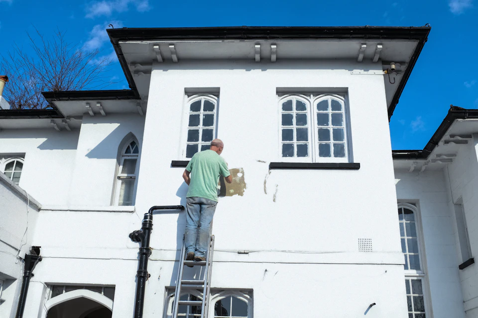 Painter on scaffolding rolling fresh paint onto a house exterior
