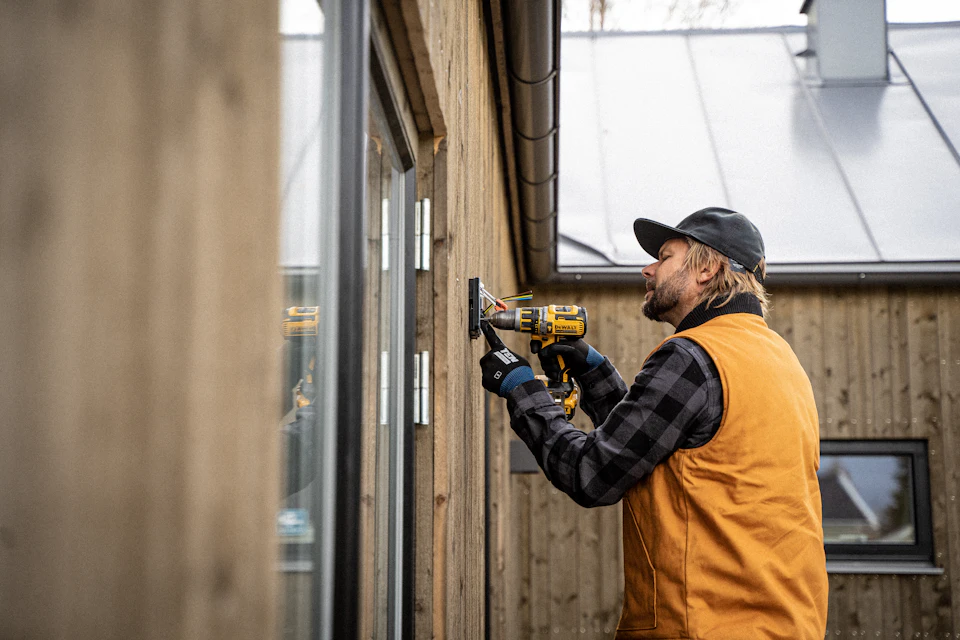 Worker drilling into an exterior wall to mount a fixture