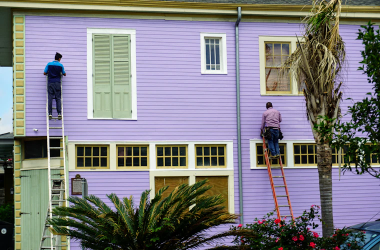 Two painters on ladders coating the exterior of a Victorian house